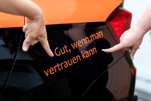 Zwei Hände zeigen auf den Schriftzug „Gut, wenn man vertrauen kann“ am Dienstwagen