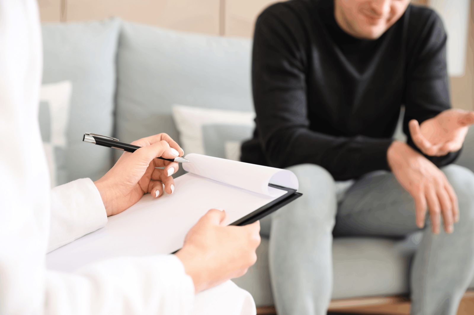 Eine Pflegefachkraft berät eine Familie auf dem Sofa und macht Notizen