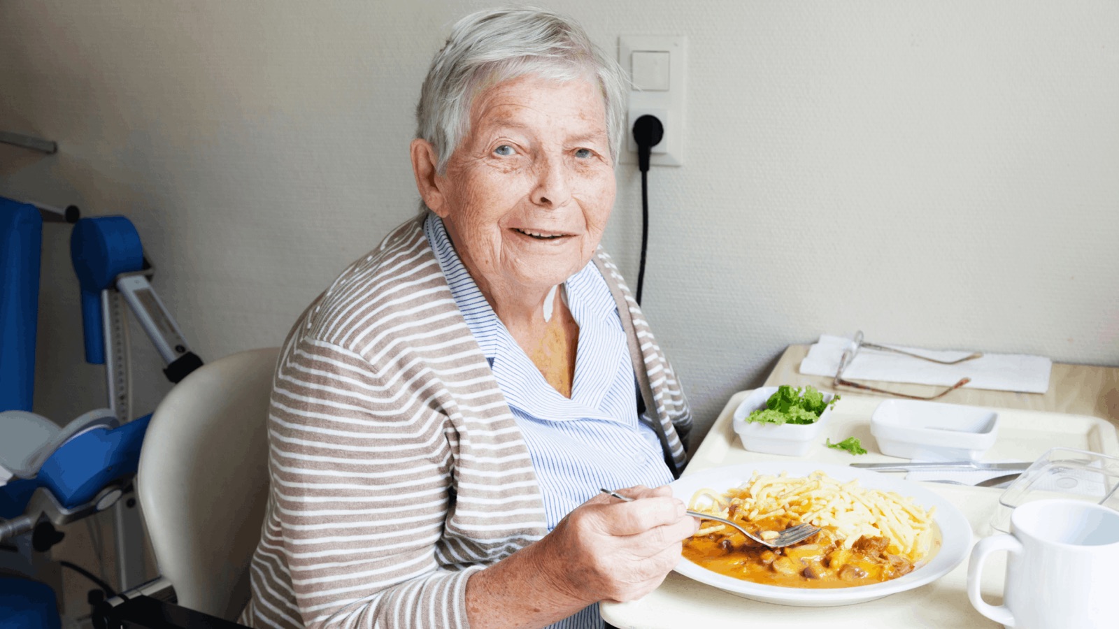 Eine lächelnde Seniorin sitzt am Tisch vor einem Teller mit Essen