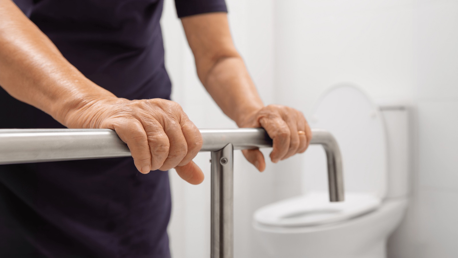 Eine Hand hält sich an einem Haltegriff neben der Toilette fest